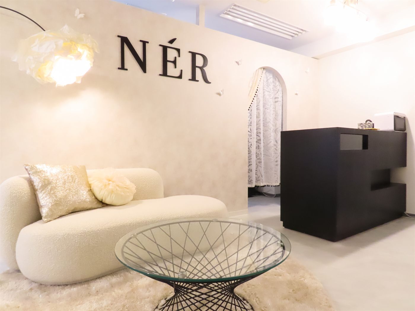 NÉRのロゴと白いソファのあるサロン